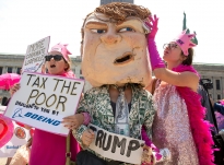 Protesters Chelsea Byers, right, of Los Angeles, pretends to use money to wipe sweat from the brow of a giant  Donald Trump head worn by Alice Newberry of Washington State. They are joined by Rebecca Green, left, of Cleveland. The women, members of "Code Pink," marched with other protesters through Public Square in Cleveland on Monday, July 18, 2016 at the Republican National Convention. Photo by Antonella Crescimbeni