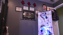 Kyle Massari holds a hockey banner made for him in his house in Trevose, Pennsylvania. Behind him, memorabilia from his hockey career hangs on his bedroom wall.